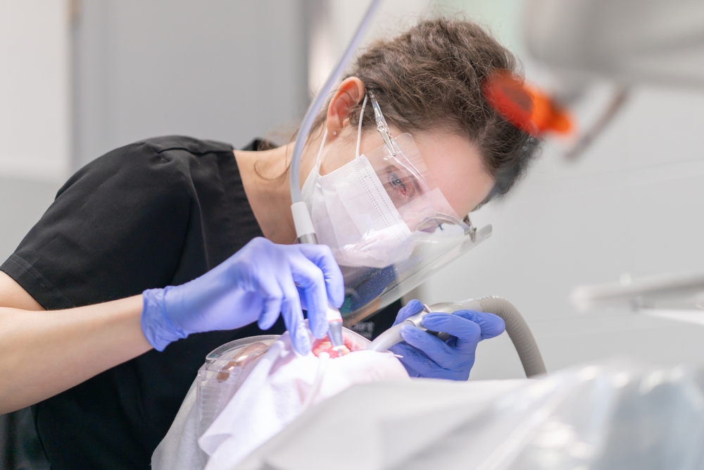 Dental Professional Performing Teeth Cleaning – Teeth Cleaning Near Me A dental hygienist in protective gear focuses on cleaning a patient’s teeth using professional dental instruments in a clinical setting – teeth cleaning near me