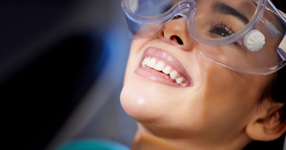 Close-Up Smile at Dentist Woman wearing protective eyewear at a dental appointment, smiling confidently. Great for dental care, safety, and oral health visuals.
