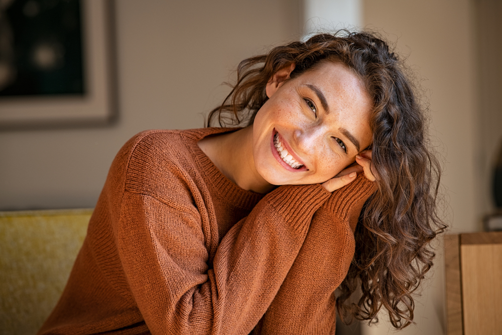Smiling Woman in Cozy Sweater - Bakersfield Orthodontist Portrait of a cheerful woman with curly hair smiling warmly in a brown sweater. Ideal for lifestyle, wellness, positivity, and natural beauty themes. - Bakersfield Orthodontist