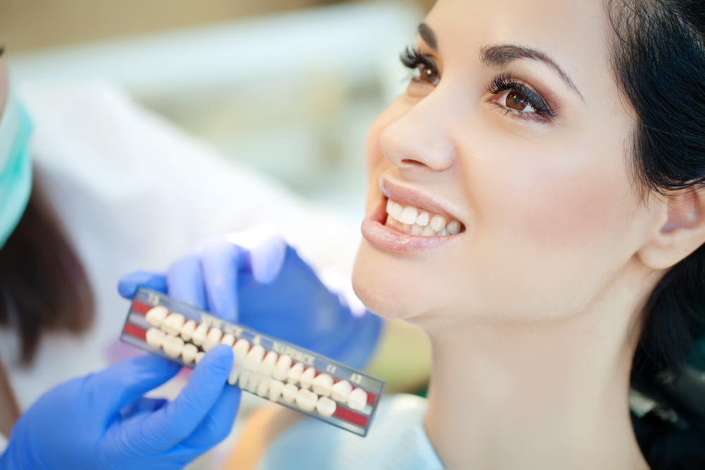 Tooth Shade Matching – Cosmetic Dentistry Consultation Woman smiling while selecting a tooth color shade at the dentist. Perfect for cosmetic dental services, veneers, and smile enhancement topics.