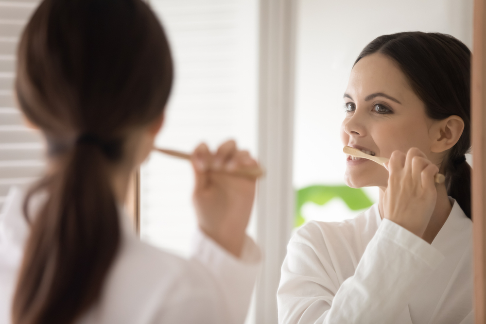 Morning Dental Routine Young woman brushing her teeth while looking in the mirror. Perfect for oral hygiene, morning habits, and dental care promotions.