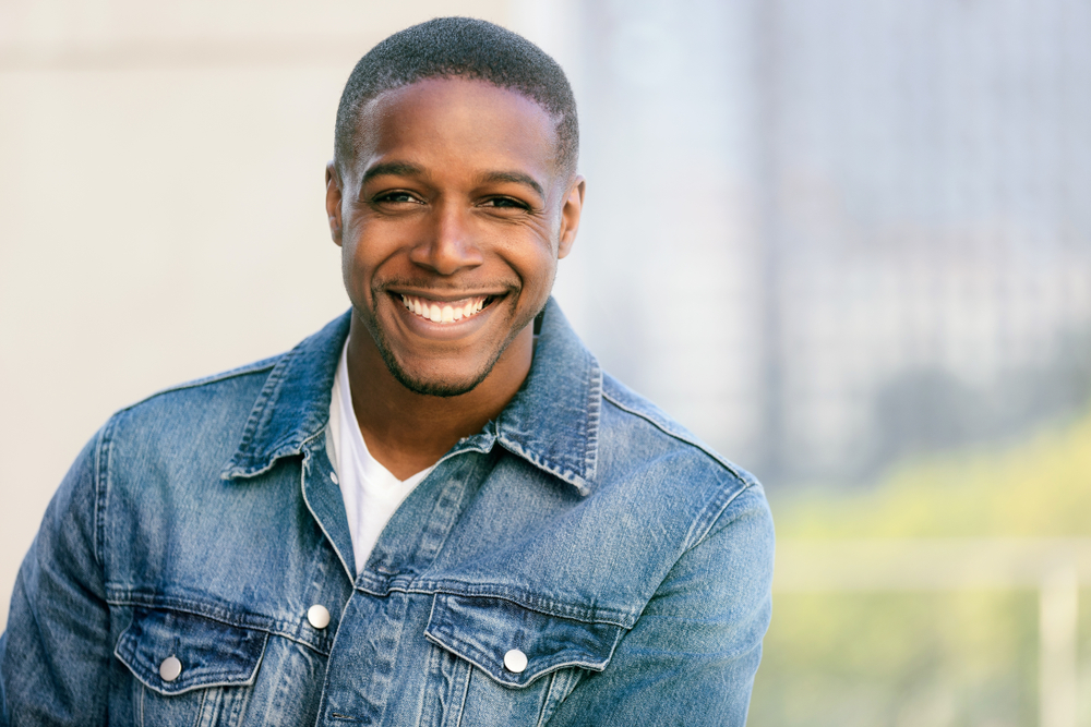 Confident Man Smiling in Denim Jacket – Casual Lifestyle Portrait - Dental Crowns in Bakersfield Friendly young man smiling outdoors in a denim jacket. Great for lifestyle, personal branding, confidence, and positivity themes. - Dental Crowns in Bakersfield