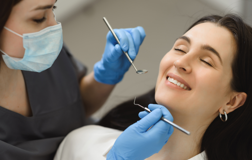 Relaxed Patient During Dental Checkup - Cosmetic Dentist Smiling woman receiving a dental exam with tools held by a gloved dentist. Perfect for promoting stress-free dental visits and professional care. - Cosmetic Dentist